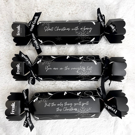 Three wrapped adult theme naughty Christmas crackers with a black and white design, featuring a bow and a card with a Christmas message.