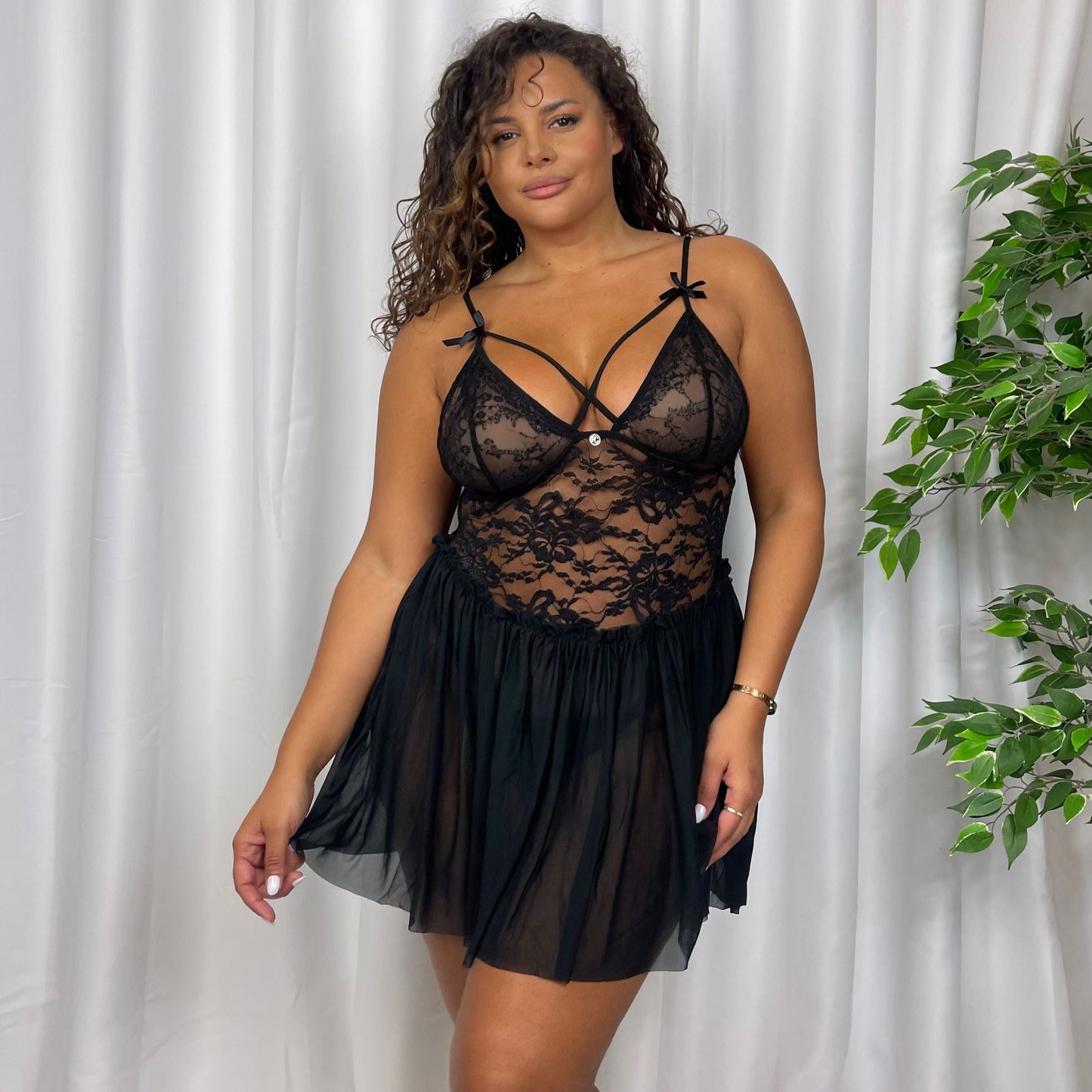 A model wearing a black babydoll lingerie set by Freak Geek brand, with strap detailing and a sheer panel, including a matching thong.